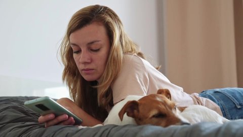 Woman at bedroom. Woman rest on the bed with her dog and using smartphone