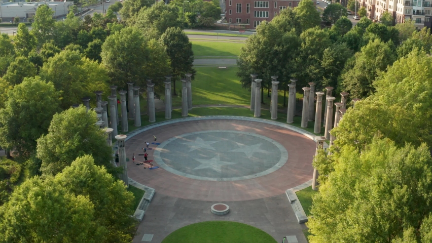 Aerial tilt down reveals carillon pillars and people doing yoga. Tennessee state emblem, logo.