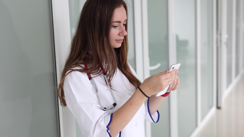 Youg female doctor using phone during break in clicic