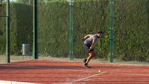 Slow motion of a man who is playing paddle tennis and fails to hit the ball with the racket. Padel match or practice on an outdoor court.
