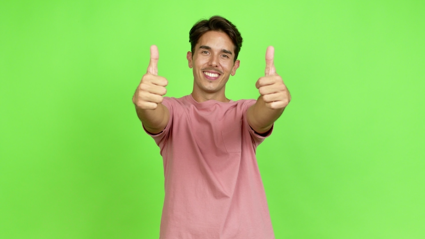 Young man giving thumbs up and smiling because something good has happened over isolated background. Green screen chroma key