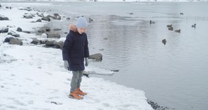 Child thrilled by outdoor activities. Boy feeding ducks on the lake. Holiday moments, childhood wonder. Winter wonderland. 4K video 