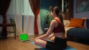 Fit young woman coach doing yoga stretching, flexing her shoulders, drinking water. Self-isolation during coronavirus lockdown, sport remote education online. Healthy lifestyle concept, home gym.