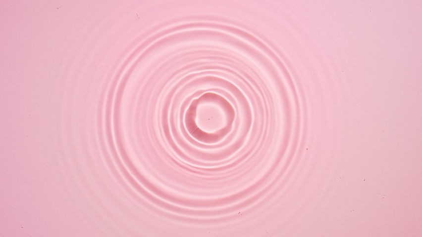Drop falls down creating circles on water surface on pale pink background | Background shot for beauty commercial