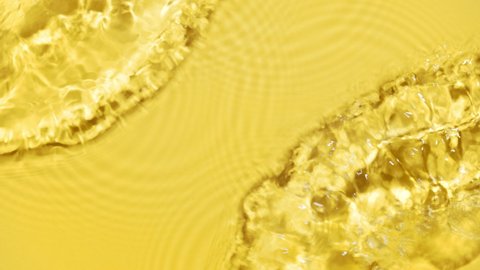 Water flows from opposite sides creating waves, ripples and bubbles on yellow background | Skin care background shot for cosmetics commercial