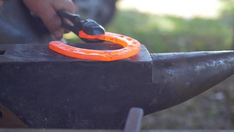 Slow motion close-up of blacksmith making a dent on red hot horseshoe 
