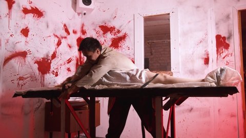 Horror acting - the doctor ties the mad girl to the table in the bloody room of mental hospital