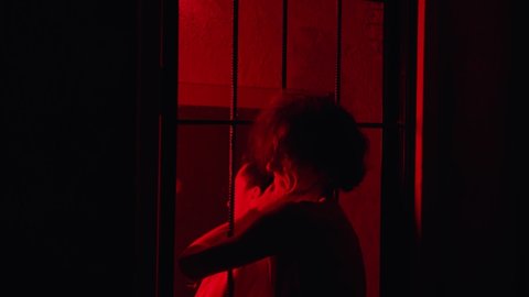 Horror acting - a male prisoner strangles the warden with his hand through the cell bars in red lighting