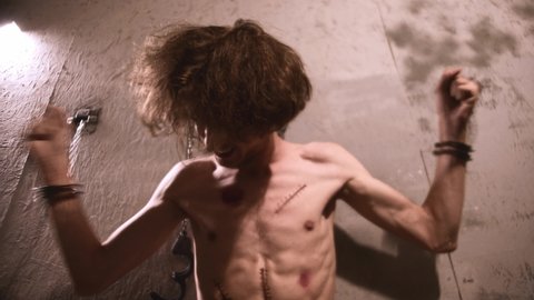 Horror acting - a shirtless man handcuffed to the wall in a psychiatric hospital cell and screaming while trying to get out