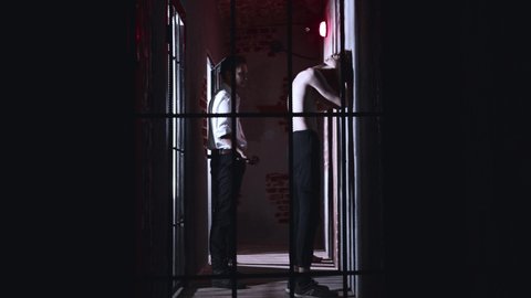 Horror acting - a dangerous male warden releases prisoners from the cell holding a metal pipe and walks them out of the corridor