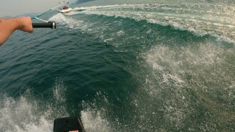 Action Sports Point of View with Man Slashing Wave on Wakeskate Behind Boat. Wakeboarding without bindings carving the wake on Lake Roosevelt Washington