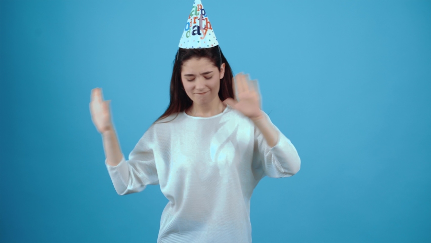 The optimistic and pretty brunette rejoices at a birthday party with a cone on her head, dancing rhythmically to the music. Asian with dark hair, dressed in a blue blouse, isolated on a dark blue