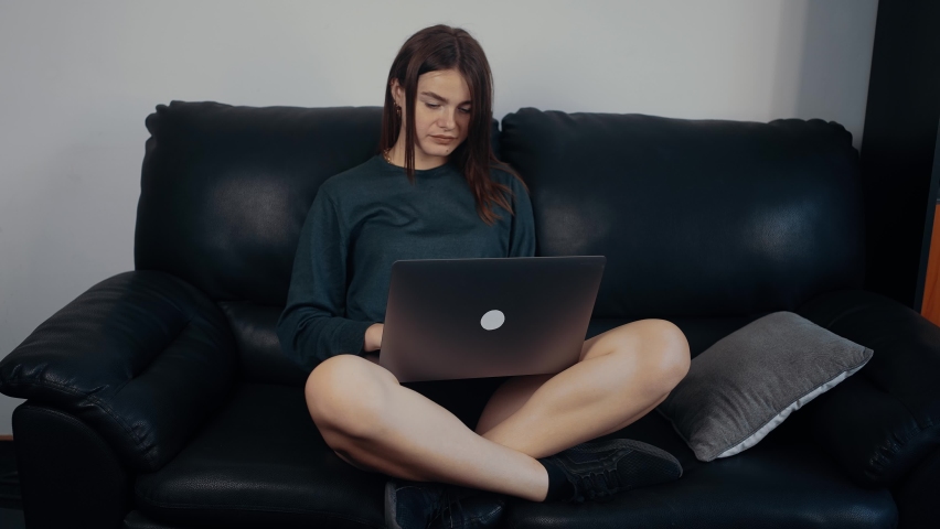 The young journalist sits on the couch with her laptop in her arms and generates new ideas for her next article. Dressed in a dark green suitcase, sitting on a black sofa. Work concept. 4k concept Royalty-Free Stock Footage #1078309625