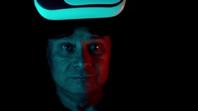 middle-aged man in a dark room with neon lights in modern VR glasses interacting with network while having virtual reality experience, concept study of parallel reality, another world