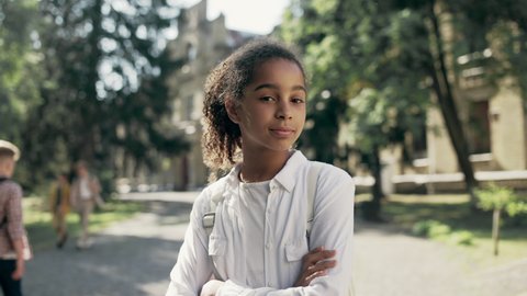 Confident biracial school girl posing on camera with arms crossed on chest