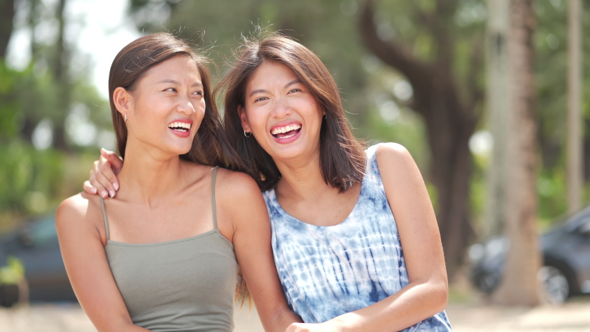 4K Portrait of Attractive Asian woman sibling sister family sitting on the beach with smiling face. Beautiful female friendship relax and enjoy outdoor activity lifestyle on summer holiday vacation.