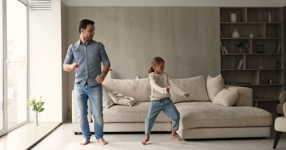 Young cheerful man have fun enjoy active dances with cute little daughter in cozy living room, full-length view. Carefree leisure time together at home, family weekend funny activities, hobby concept Royalty-Free Stock Footage #1078337957