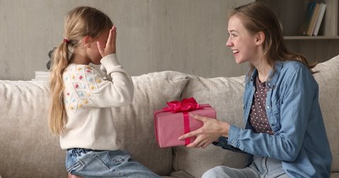Little girl cover her eyes with palms anticipate long-awaited present received from loving mother. Woman give gift box to daughter on her Birthday, express care and love. Life events, congrats concept