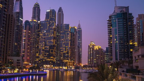 Dubai, UAE - July 2021: View of Dubai Marina promenade with yachts and modern Towers with restaurants from bridge in Dubai night timelapse, United Arab Emirates.