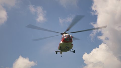 Low angle of red and white helicopter with large propeller flying in cloudy blue sky during emergency operation
