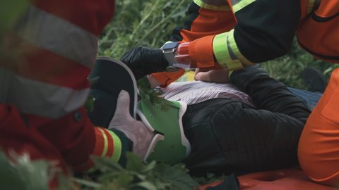 Anonymous doctors taking off neck brace from unconscious man during rescue operation in field
