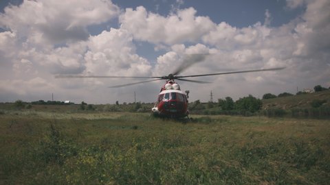 Emergency service helicopter with spinning propeller landed in grassy field during rescue mission on cloudy day