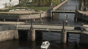 Daylight shot of old bridges and people strolling along in the road. White boat sailing on a urban river, spring time in a city with historical sights, top view gimbal shot