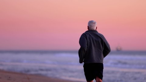 64 year old man getting his exercise at the beach at sunset. Slow Motion.