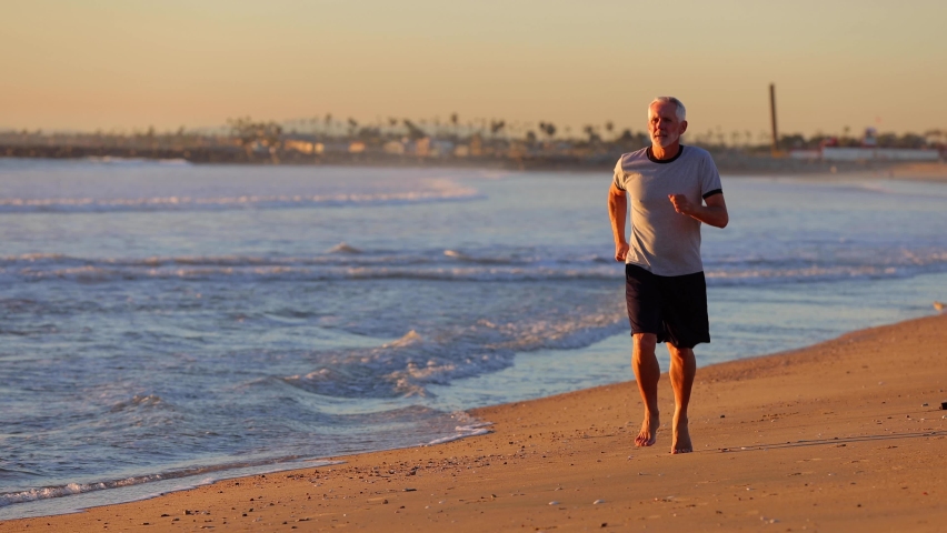 64 year old man getting his exercise at the beach at sunset. Slow Motion.