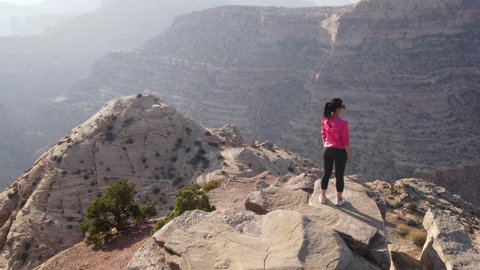 Aerial shot of an Asian woman hiking along the edge of the San Rafael River Canyon in Utah also called the Little Grand Canyon