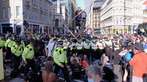 LONDON, UK – August 27, 2021: XR Protesters Block Central Intersection and erect bamboo structures while being surrounded by Police at Extinction Rebellion Blood Money Protest, London, England, UK