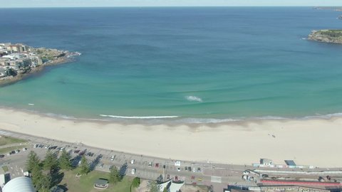 Aerial shot of Bondi Beach on a sunny day in Sydney, Australia. Drone flying backward to capture beautiful turquoise water and sandy beach