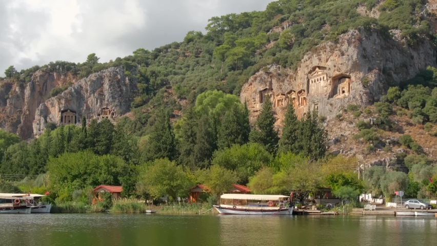 Rock-cut temple tombs of the ancient city Kaunos in Dalyan, Mugla, Turkey. Beautiful Dalyan river view with ferry boats and carved tombs at background.