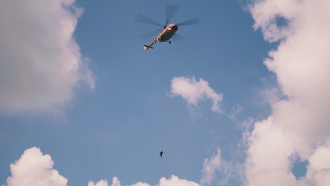 From below modern helicopter with fire extinguisher flying against white clouds in blue sky during emergency situation in nature