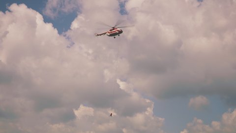 From below emergency service helicopter with fire extinguisher flying in cloudy blue sky during rescue operation