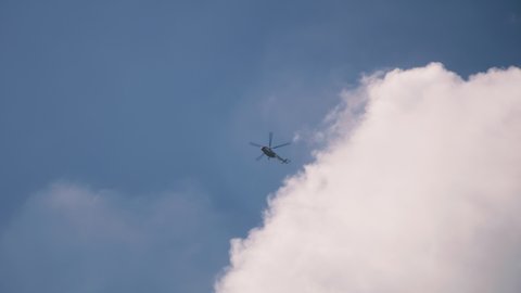 Tracking shot of helicopter flying high in cloudy blue sky against bright sun in daytime