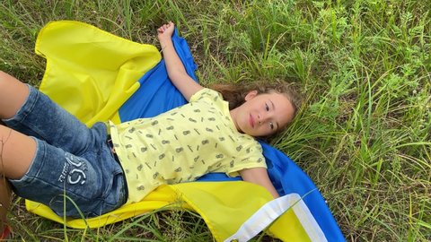4k Smiling small girl lies on Ukrainian flag in the meadow