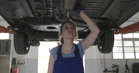 Confident female mechanic in a repair shop, she is working under a car, women's employment concept