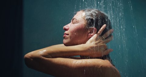 Cinematic shot of  young carefree sensual brunette woman is taking hot relaxing shower in a luxury wellness center. Concept of femininity, personal hygiene, spa center, freedom, skincare, healthcare.