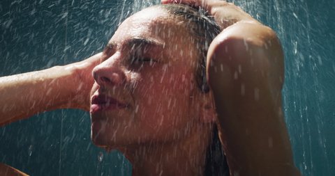 Cinematic shot of  young carefree sensual brunette woman is taking hot relaxing shower in a luxury wellness center. Concept of femininity, personal hygiene, spa center, freedom, skincare, healthcare.