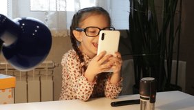 The little girl with glasses takes pictures of the blog. Video conference. Communication at a distance. Quarantine. The child grimaces at the camera.