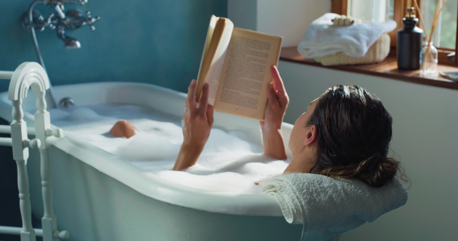 Cinematic shot of young woman reading book while relaxing with pleasure in foamy bubble filled perfumed bathtub at home. Concept of leisure, education, rest, comfort, skincare, healthcare. Royalty-Free Stock Footage #1078368947