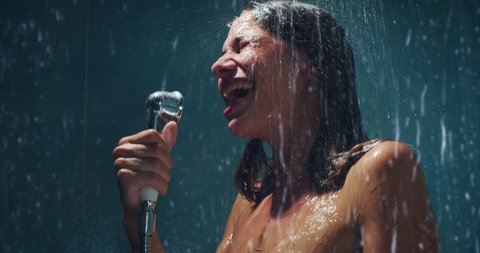 Authentic shot of carefree woman having fun to sing her favorite song with shower handle and dance crazy while taking relaxing shower at home. Concept: freedom, happiness, leisure, pleasure, skincare.