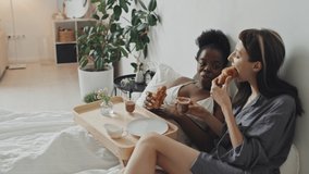 Handheld slowmo of Caucasian and African-American women sitting on bed in cozy apartment and enjoying breakfast - Powered by Shutterstock - Get 15% off with code: PIKWIZARD15