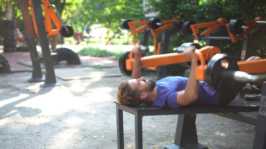 Open air gym. Street training on the municipal sports simulators. Athletic man doing bench press using outdoor training machine. Royalty-Free Stock Footage #1078373345