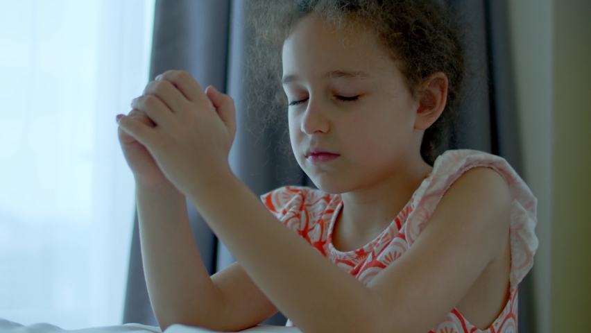Little girl is praying in her room.Close up portrait of child concept faith religion and happy family.Child daughter crossed her arms, praying to god.Catholic pray worship and gratitude.