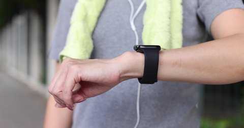 Woman runner wearing smartwatch and using a finger to touch screen for setting program for new running session and when finish she start to run and fade in blur background in outdoor city park.