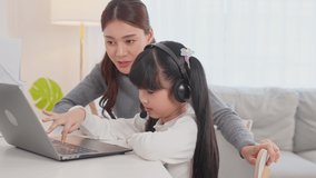Asian little young girl kid learning online class at home with mother. Preschool child use laptop computer do homework, homeschool from school teacher by digital remote internet with support from mom.