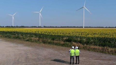 Wind turbines in sunflower fields, engineers in special clothing monitor the operation of wind turbines, aerial footage.