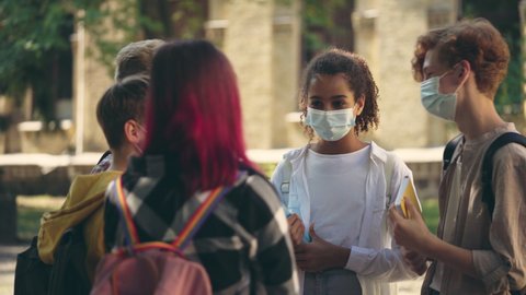 Multiethnic school kids in protective face masks talking after classes, pandemic